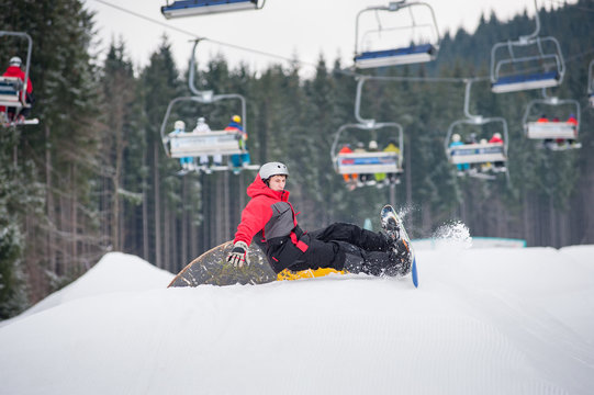 Snowboarder falls on the slopes during the jumping with ski lifts in background, extreme sport, Bukovel, Ukraine