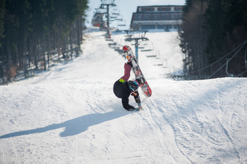 Snowboarder in the moment of falling on the snowy slope overlooking a ski lifts and a ski run at a...
