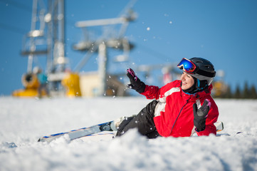 Smiling girl skier lying with skis on snowy at mountain top and throws snow in sunny day, having fun at a winter resort, ski lifts and blue sky in background. Bukovel, Ukraine