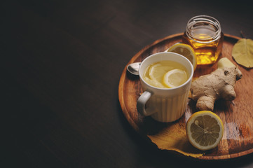 cuisson du thé chaud au gingembre, au citron et au miel dans un intérieur rustique sombre. Ingrédients et tasse sur fond de bois