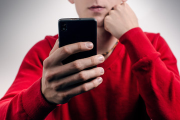 Businessman using a mobile phone indoor.Detail of hands and phone. Red sweater. Grey background. Technology concept. Young man
