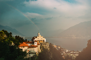 Stormy rainbow view of Madonna del Sasso Church above Locarno city, lake Maggiore (Lago Maggiore) and Swiss Alps in Ticino, Switzerland.
