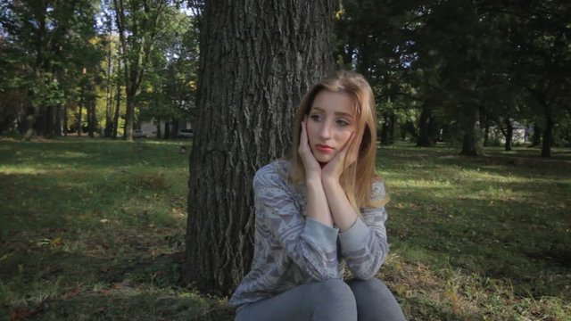 Lonely girl in sports form is bored sitting under a tree in the park