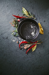 Cast iron pan, spices and herbs on a black stone