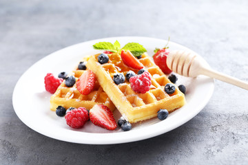 Homemade waffles with berries in plate on grey table