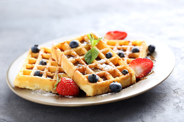 Homemade waffles with berries in plate on grey table