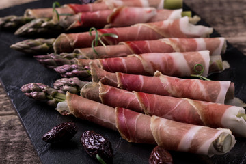 Fresh organic asparagus wrapped in Parma ham on a cutting board