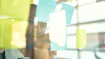 Two creative millenial small business owners working on social media strategy brainstorming using adhesive notes in windows