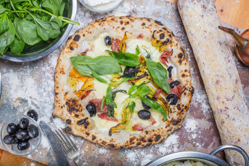 Traditional italian pizza with mozzarella, salami, ricotta and pumpkin flowers on black chalkboard