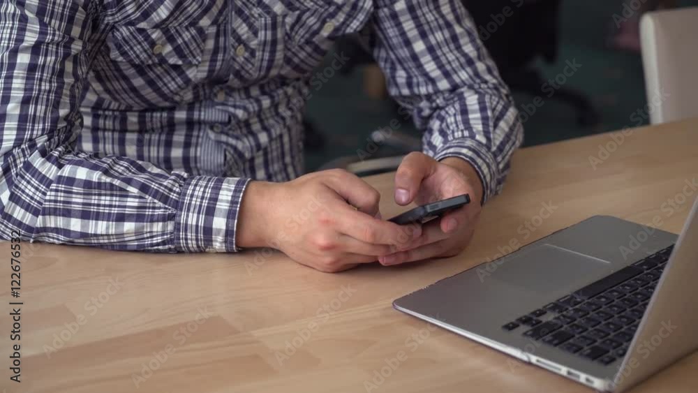 Poster busineman's hands texting message on smartphone. guy sitting at the wooden desk with computer in the
