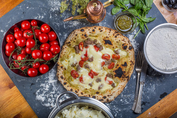 Traditional italian pizza with tomato, salsicia and pesto on a black chalkboard