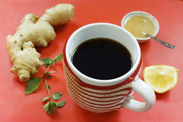 Health Care concept: hot ginger tea in a warm cup, lemon, mint and honey on a red background