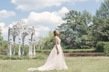 Beautiful tender young woman bride in her wedding dress gentle air walks in the lush garden on a hot sunny summer day