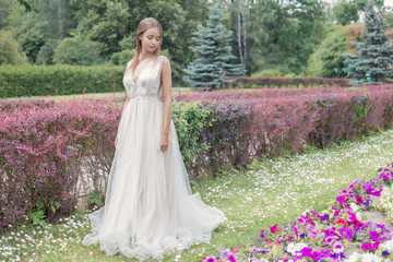 Obraz na płótnie Canvas Beautiful tender young woman bride in her wedding dress gentle air walks in the lush garden on a hot sunny summer day