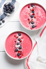 Strawberry and beetroot smoothie bowls topped with blueberries, chia, pomegranate seeds and shredded coconut. Top view