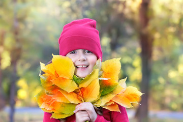 Happy child girl with autumn leaves outdoors.