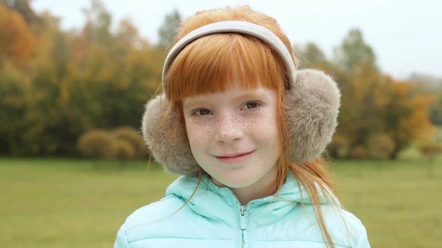 Close up little redhead girl in the earmuffs in the park