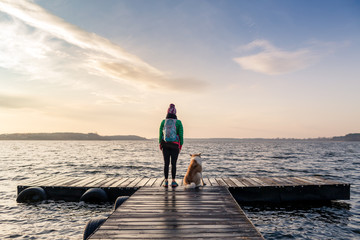 Woman with dog enjoy sunrise at lake, backpacker looking at beautiful morning view