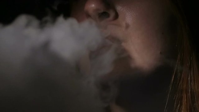 Young woman smoking electronic cigarette on black background