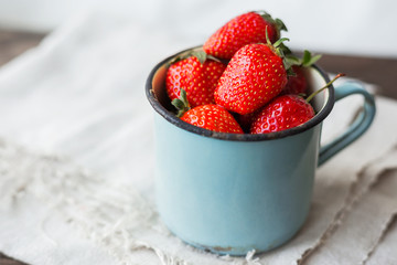 Fresh juicy strawberries  in old rusty mug. Rustic wooden background with homespun napkin.