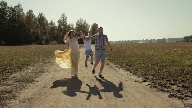 Smiling laughing family running at the field. Parents lift their son up