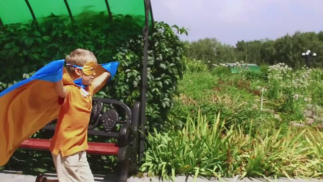 Young boy dressed as superhero playing outdoors. Kid wearing superman cape running in the park.