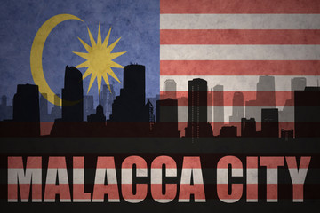 abstract silhouette of the city with text Malacca City at the vintage malaysian flag background