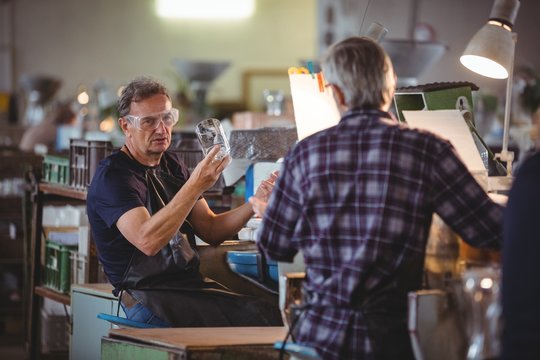 Glassblower showing glass vase to a colleague
