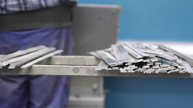 Pracownik obrabia profile z metalu i odkłada je na gromadkę