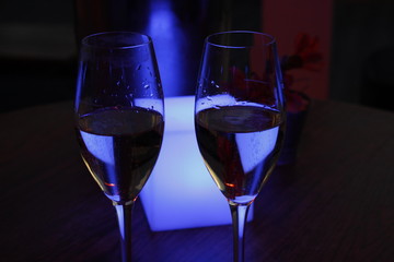 Two glasses of champagne in front of a blue light cube in a champagne lounge at night