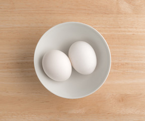 Two eggs in a bowl atop a wood table top.