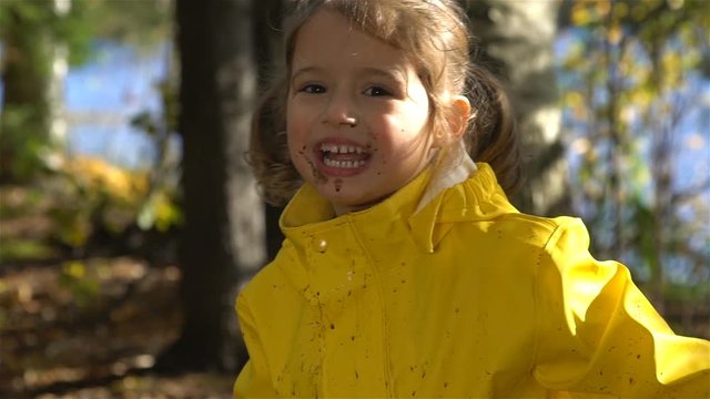 Little funny girl with a dirty face is jumping in a dirty puddle. Slow motion.
