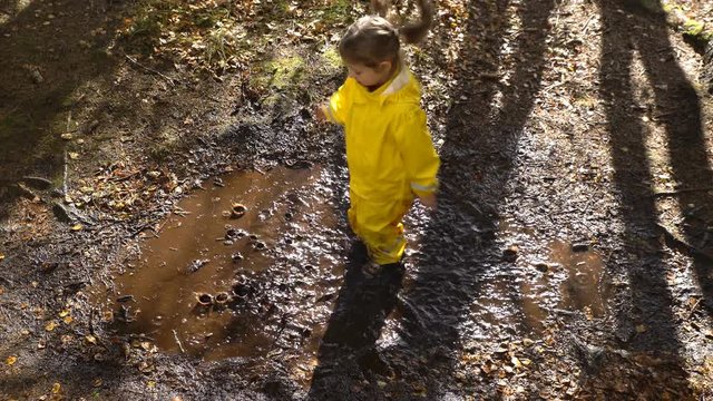 Little girl in a yellow rubber suit is jumping in a puddle.
