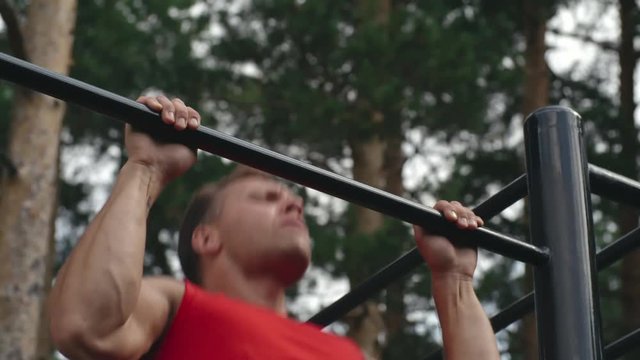 Slow motion shot of man using overhand grip while doing pull ups outdoor