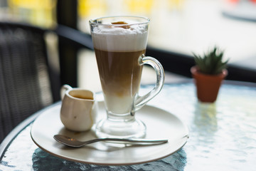 hot fresh latte coffee cream in see through glass and white shinning latte coffee in pot with silver spoon on glass table at coffee time pourred already/ hot fresh coffee