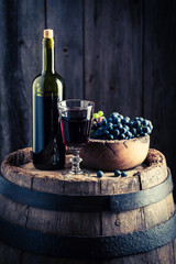 Delicious red wine with fresh grapes on wooden barrel
