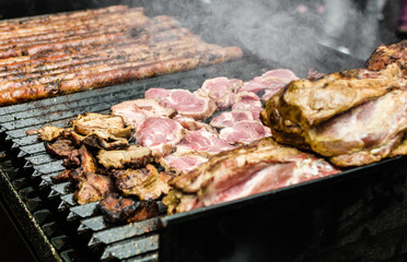 Argentina barbecue asado chorizo sausages and meat cooking on parilla grill at a street food market