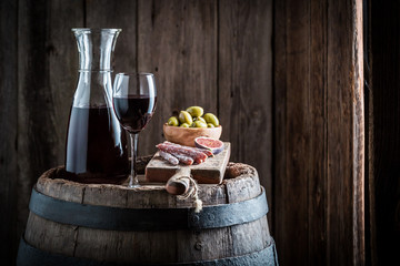 Fresh red wine with cold meats and olives on old barrel