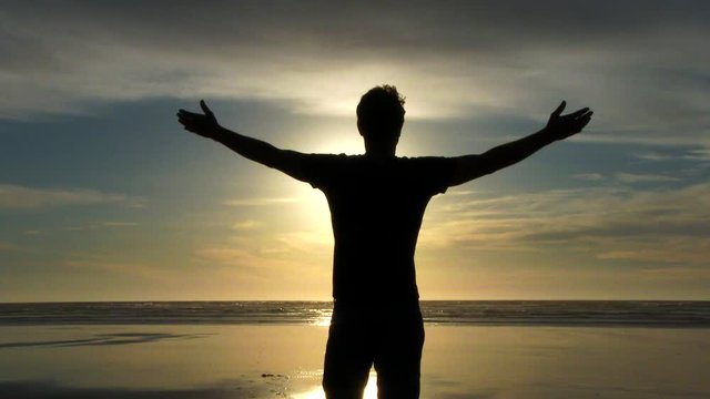 Model released person standing with arms up in the air on sandy beach shoreline catching some rays and enjoying the breeze at the Pacific Coast in Oregon.