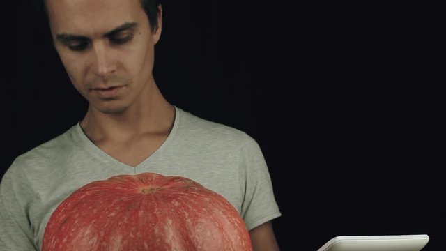 Guy in white shirt use picture on tablet computer as reference and draw on pumpkin with a marker