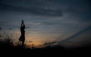 Silhouette of a young woman practicing yoga at sunset