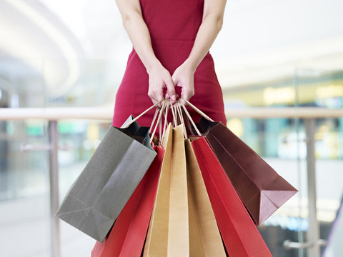 young woman carrying shopping bags standing in mall, focus on the hands