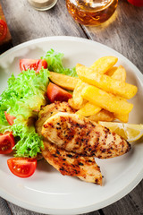 Grilled chicken breasts served with fries and fresh salad