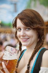 Portrait of cheerful young German woman wearing traditional dirndl and holding a beer mug at Oktoberfest