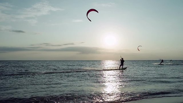 Kitesurfing. Silhouettes of five surfers riding on boards on the surface of waves at sunset. Azov sea. HD