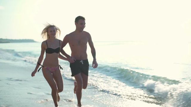 happy couple in swimwear running along the seashore slow motion