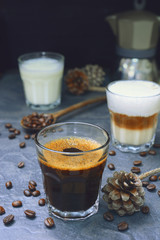 glass of hot espresso and cappuccino coffee with creamer, glass of milk and moka coffee pot on a rustic stone board.