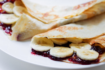 Obraz na płótnie Canvas Thin pancakes with cherry jam and banana slices on a white plate