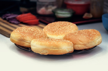 Four buns with sesame seeds for burgers on the plate on the kitchen table. Cooking burger concept