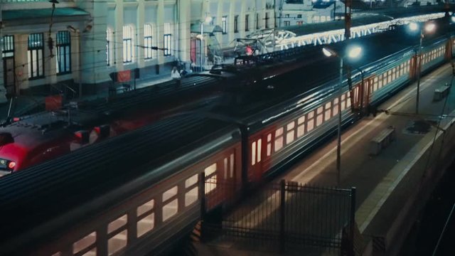 RUSSIA MOSCOW STATION - SEPTEMBER 2016: Passenger train slowly leaves from railway station at night, people walking nearby on the background.